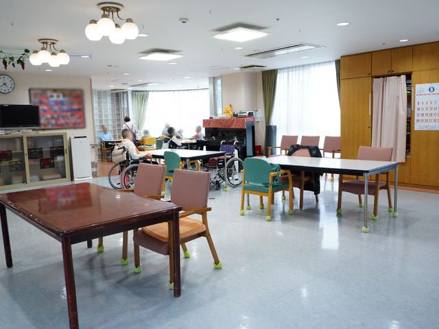 共有スペースの様子 食堂 椅子が並べられた開放的なダイニングルームです。利用者が安楽な姿で過ごしており、共同生活の温かみを感じさせます。