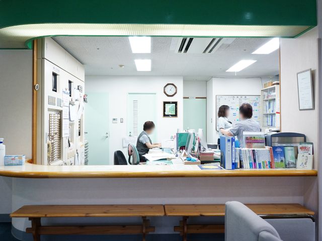 フロントスタッフと書類 受付 フロントのスタッフが書類に目を通し、来訪者の対応に忙しそうです。コミュニケーションを大切にする環境が垣間見えます。