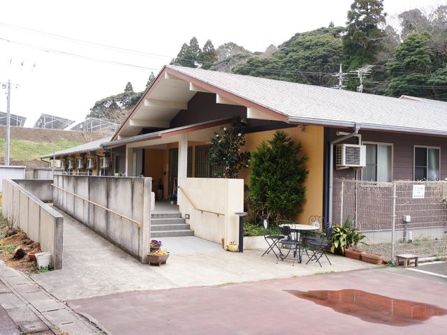 施設の外観 玄関 緑豊かな環境に佇む一階建ての施設です。段差の少ない設計で、どなたでも安心してお越しいただけるようになっています。