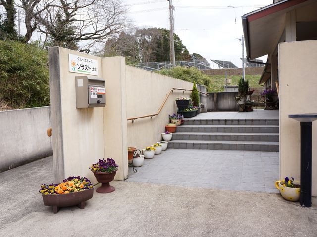 エントランスの花と階段 外観 階段に沿って設置された花々が、来訪者を温かく迎え入れるエントランスです。無理のない段差で安全に配慮されています。