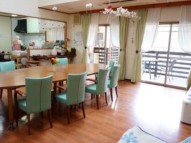 明るい共有ラウンジ空間 食堂 広々としたダイニングルームでは、作業に勤しむスタッフの姿があり、利用者様が食事やコミュニケーションを楽しめる優しい雰囲気です。