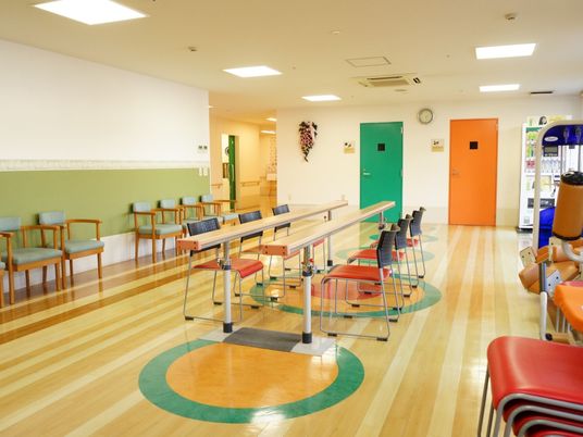 部屋の中央に縦長の板が２本設置されており、椅子が３脚ずつ置かれている。周囲の壁にも椅子が並べられている。