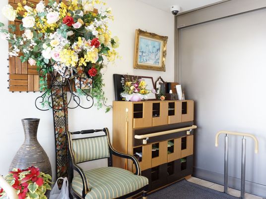 部屋の一角に、スタイリッシュな下駄箱が置かれている。下駄箱の上や近くには、造花が華々しく飾られている。下駄箱の隣に、椅子がある。