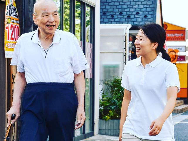 笑顔で歩く高齢者と職員 職員の温かなサポートが光る散歩風景です。明るく穏やかな雰囲気が、日々の業務に対する情熱を伝えています。