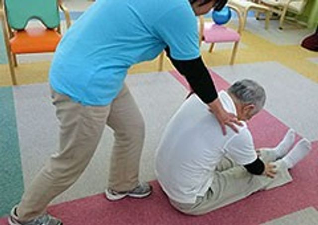 ストレッチをする室内 機能訓練室 利用者の方がリハビリを行う様子です。専門スタッフが丁寧にサポートしています。