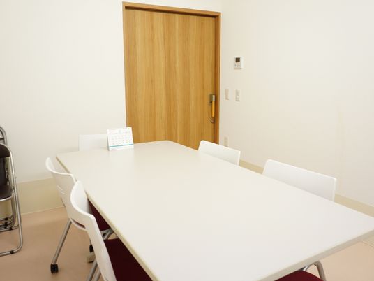 白いテーブルと椅子が置かれている。椅子はキャスターが付いている。パイプ椅子も壁側にある。扉は大きく引戸になっている。