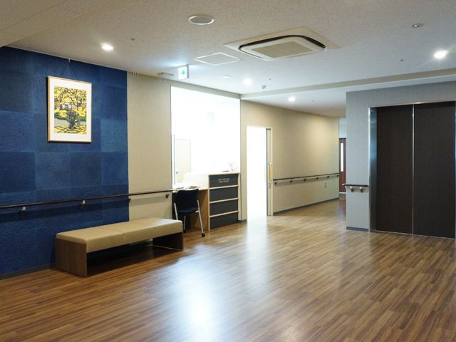 明るい廊下と掲示物 エレベーターホール シックな色合いのベンチが置かれ、休憩にも適した落ち着いた雰囲気の廊下です。