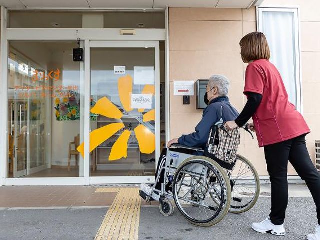 車椅子でエントランスへ エントランス 車椅子で外出から戻る方と、手厚いサポートを提供するスタッフが確認でき、笑顔での対応が伺えます。