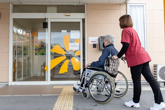 車椅子でエントランスへ エントランス 車椅子で外出から戻る方と、手厚いサポートを提供するスタッフが確認でき、笑顔での対応が伺えます。