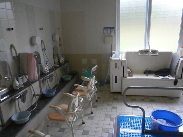 浴室の介助用設備 浴室   手すりや椅子が備わった浴室です。明るい窓辺に、洗い場と入浴補助機器が整っています。