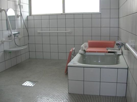施設の写真 窓や壁に手すりが設置された浴室である。完備されている浴槽には、入浴介助の器具が設置されている。入居者様には安全に入浴していただける。