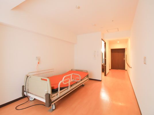部屋内のドアはスライド式で傍には手すりがある。車輪で移動可能な介護用ベッドが備え付けられており、間口幅も広めにとられている。