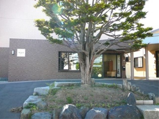 エントランスの風景 中庭 広々とした空間に緑も豊かな入り口は、訪れる方々を温かく迎え入れます。澄み切った青空の下、穏やかな時間が流れている様子が感じられます。