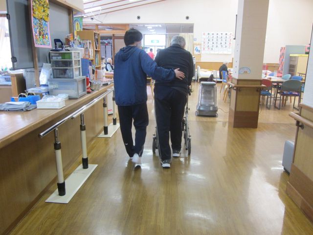 優しい介助を受ける廊下 廊下   職員が入居者の方に寄り添いながら歩行をサポートしています。明るく広々とした施設です。