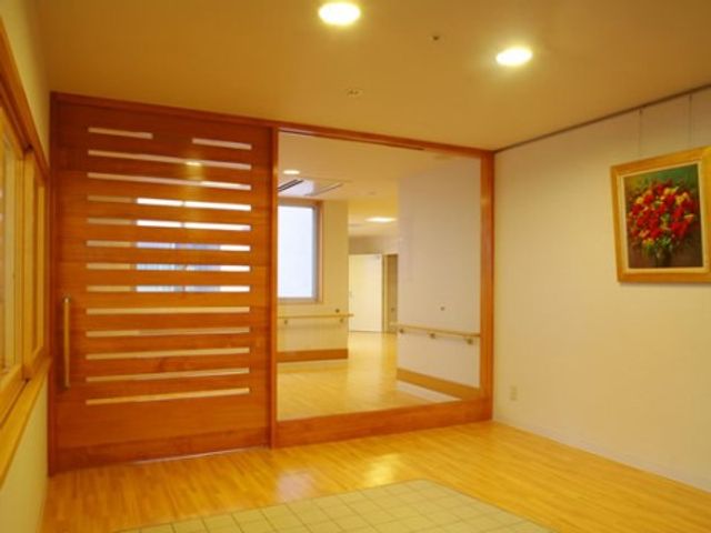 明るい廊下と木製扉 エントランス 柔らかな照明で照らされた落ち着いた雰囲気の廊下です。木製のスリット扉が上品な印象を与え、ゆったりとした空間が広がっています。