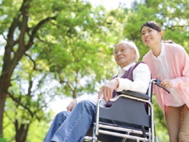 植物と車椅子の散歩 入居者様 散歩を楽しむ笑顔の利用者様とスタッフが、自然豊かな環境の中で潤いの時間を過ごしています。