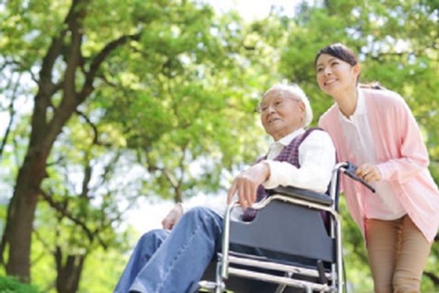 植物と車椅子の散歩 入居者様 散歩を楽しむ笑顔の利用者様とスタッフが、自然豊かな環境の中で潤いの時間を過ごしています。