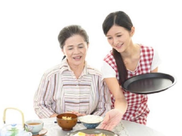 笑顔で食事サポート 入居者様 温かい配膳を受ける笑顔の利用者様と、丁寧な対応を心がけるスタッフの姿が印象的です。
