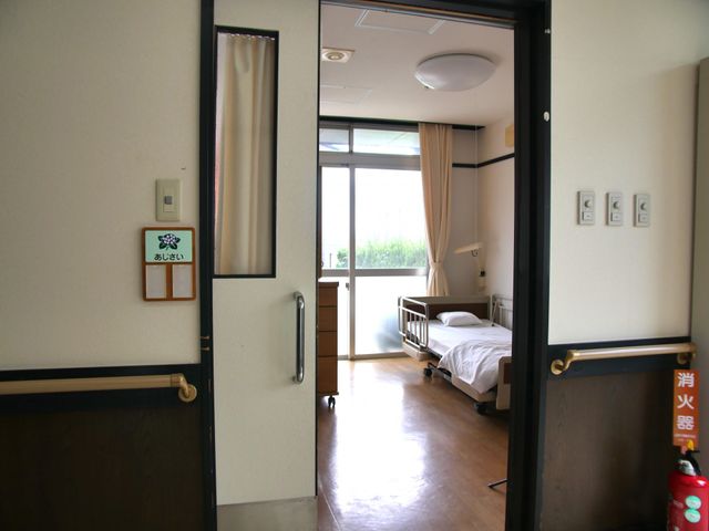 居室の入口 居室 ゆったりとした入口の居室です。柔らかい光が差し込む窓と、清潔感のあるベッドが配されています。