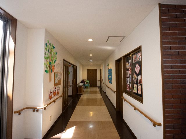 廊下に掲示物がある様子 廊下B 手すり沿いに明るい廊下が続き、壁には季節感のあふれる掲示物が飾られ、訪れる人を和ませます。