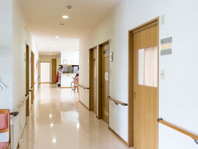 廊下に車椅子の人 廊下 廊下は広々としており、車椅子の方もゆったりと移動ができる設計です。明るく清潔感のある環境で、安心して働ける空間が広がっています。