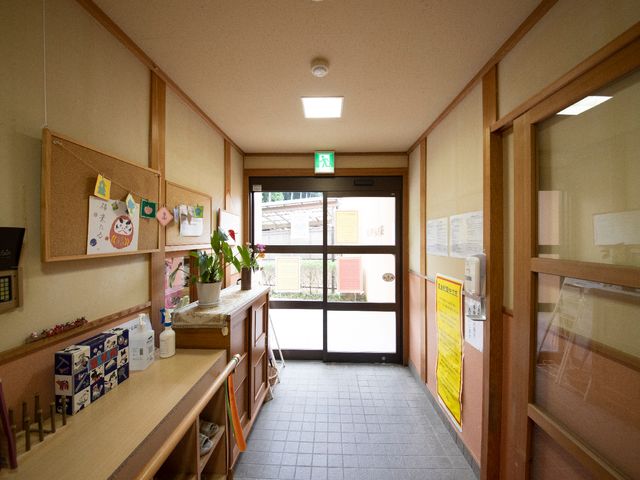 エントランスの手前の廊下 玄関ホール 居心地の良い環境が特徴的な出入り口付近です。壁には掲示物や植物が飾られ、訪れる方々を温かく迎えています。
