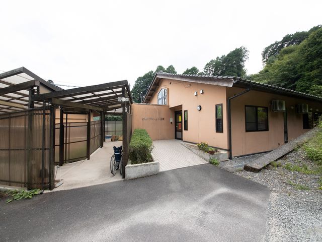 緑に囲まれた建物の外観 外観 自然豊かな環境に佇む施設前の景観です。車いすが置かれた閑静な雰囲気が感じられます。
