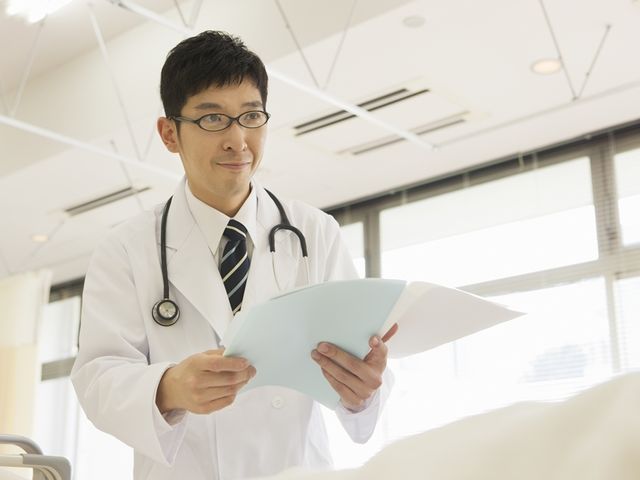 医師がカルテを確認 明るい空間で一人の医師が患者のカルテを熟考しています。専門的なケアが必要な方にも安心の対応を期待できる環境です。