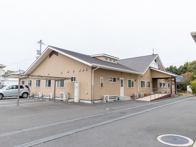 ベージュの外壁の建物外観 外観 広々とした敷地に佇む落ち着いた風合いの建物です。バリアフリー設計のエントランスが、安全で快適な職場環境を提供しています。