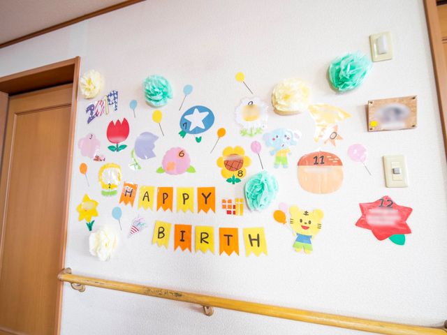 壁面の誕生日飾り付け お誕生日 壁には彩り豊かな誕生日のお祝いが飾られ、訪れる方々の目を楽しませています。ケアを大切にする温かい雰囲気をご実感ください。