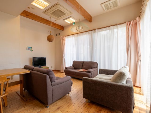 居心地の良い居室 共有スペース 温かみのある木の天井と柔らかい光が射し込む居室です。くつろぎやすいソファやテレビが配されています。