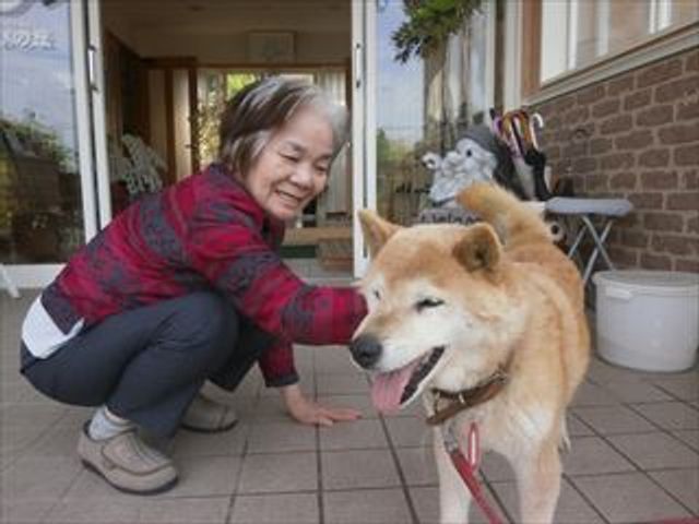 笑顔で犬と触れ合う人 エントランスにて、笑顔の方が愛らしい犬と楽しそうに触れ合っています。明るい表情からは、あたたかな雰囲気が感じられます。