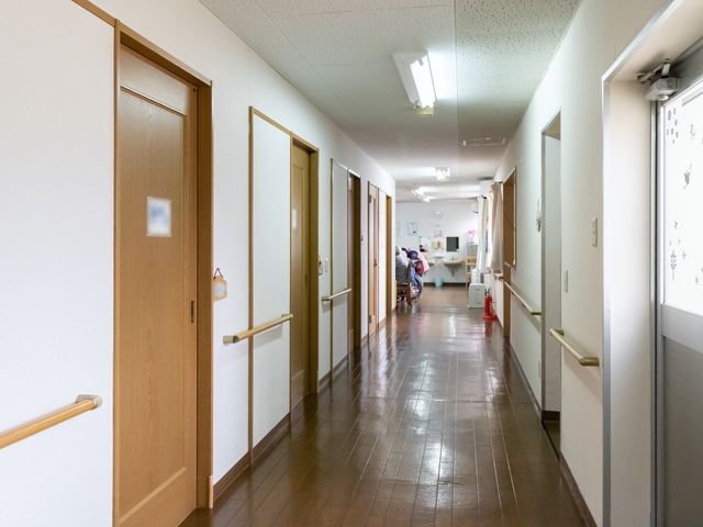 清潔な廊下と掲示物 廊下 手すり沿いに明るく広がる通路です。背後には活動的な雰囲気のスタッフが確認できます。