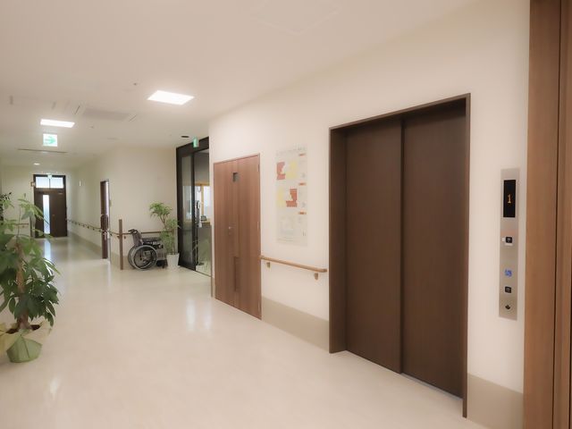 明るい廊下のエレベーター 廊下 広々とした廊下には、車椅子が置かれており、見通しの良い環境です。エレベーターも使いやすい位置にあります。