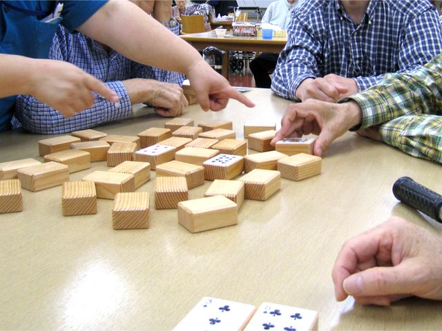 みんなで楽しむゲームの様子 多目的室 参加者がテーブルを囲み、木製ブロックのゲームを楽しんでいます。和やかな交流が見られます。