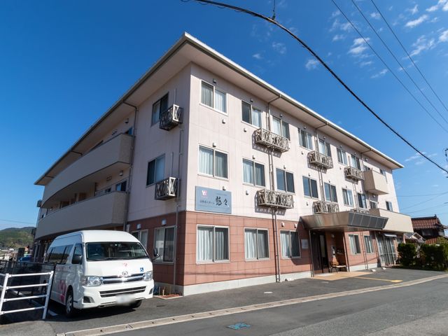 明るい日差しの居宅建物 外観 優しい色合いの外壁が印象的な明るい建物です。すぐ近くには便利な送迎用の駐車スペースも整備されています。