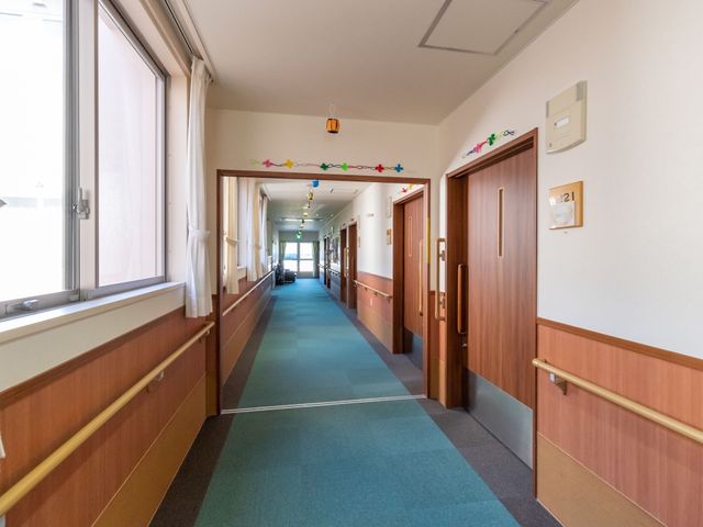 廊下の明るい風景 廊下 床から壁にかけての優しい色合いが心地よい、明るく清潔な通路です。手すりが設置されており、安全に歩行できる配慮がされています。