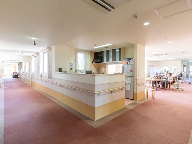 広々とした明るい廊下 キッチン 広々とした廊下は日差しが差し込み、清潔感があります。一角にはゆったりとした空間で談笑する人々が見えます。