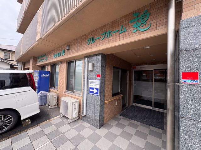施設の玄関外観です 外観   落ち着いた色合いの建物正面で、出入口は段差が少なく見えます。看板も見え、来訪時の動線を確認しやすい外観です。