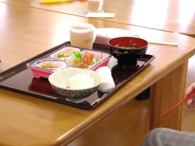 食事風景ダイニング ダイニングルーム おいしそうな和食が並ぶテーブルで、入居者の方が箸を使って食事を楽しんでいます。