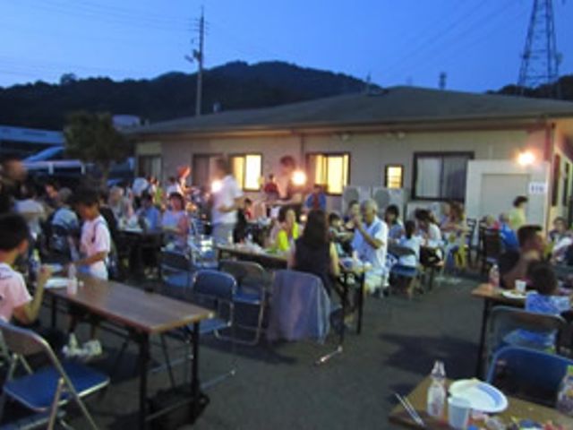 夜間の宴会風景 多目的室 夕暮れ時に開かれている集いの風景です。屋外に設置されたテーブルで、参加者同士が和やかに交流しています。