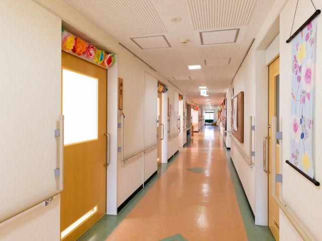 明るく広い廊下 通路 手すりが整備された安全な廊下です。壁には花の絵や装飾が施され、温かみのある空間を提供しています。