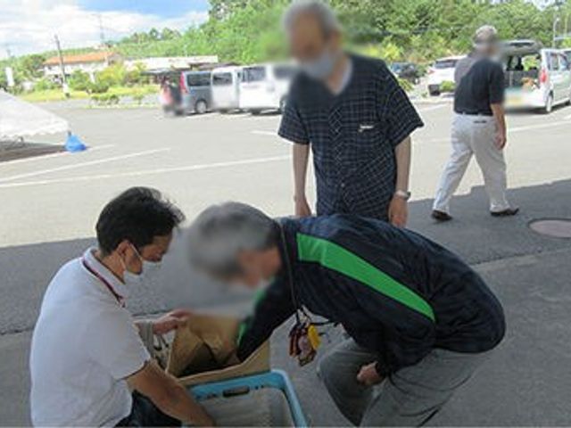 集まる人々の様子 外観 スタッフと入居者らが集まり、外で荷物を確認する交流の場です。和やかな雰囲気が感じられます。