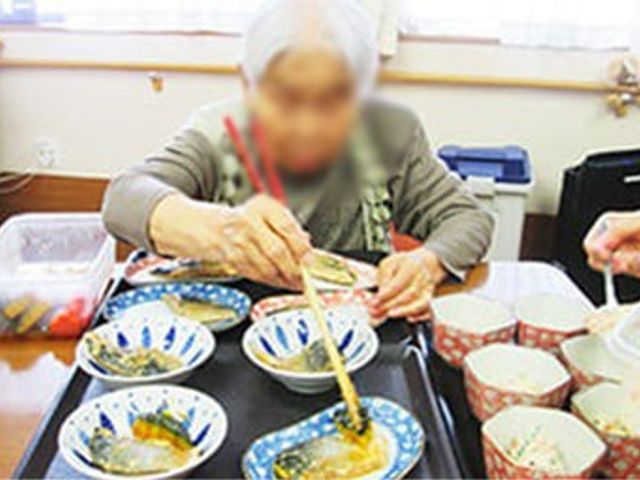 食事準備の様子 ダイニングルーム 利用者が食事の準備に参加しています。温かみのある空間で、穏やかな時間が流れています。