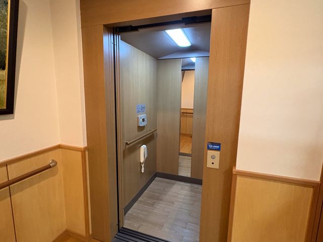 木目調の閉じた空間 エレベーター 温かみのある木目調で落ち着いた雰囲気のエレベーターです。手すりが設置されて安全性も考慮されています。