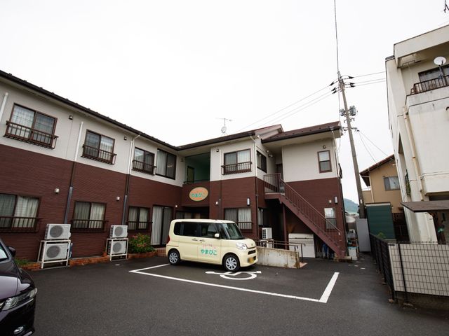 赤茶色の建物の外観 駐車場 落ち着いた色合いの建物は、清潔感があり、快適な環境での業務が期待できます。