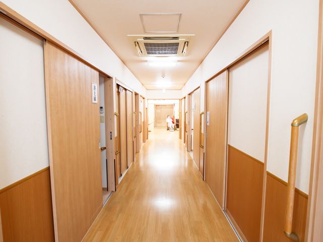 清潔感のある明るい廊下 通路 すっきりとした廊下はゆとりのあるスペースで、安全な手すりも整っています。端に座る方々が穏やかなひとときを過ごしていらっしゃいます。