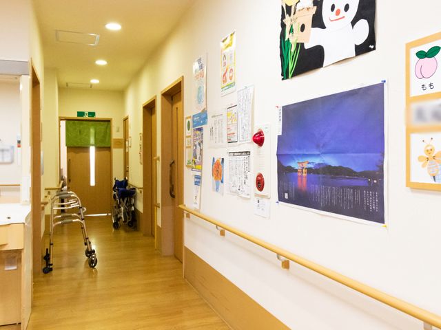 廊下に掲示物と歩行器 廊下 手すりが整った廊下には、彩り豊かな掲示物が飾られ、居心地の良い雰囲気を演出しています。歩行器が一つあり、安全に配慮された設計です。