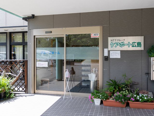 明るい施設のエントランス 玄関 植物に囲まれた清潔感のある入口です。AED設置で安心して勤務ができる環境が整っています。