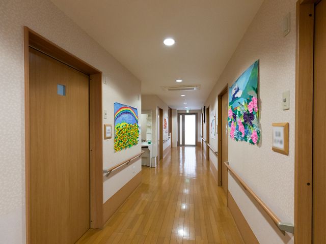 廊下の明るいアート壁面 廊下 壁に飾られたカラフルな絵画が、日々の通路を明るく彩ります。清潔感のある床と、手すりが配置された安心の設計です。